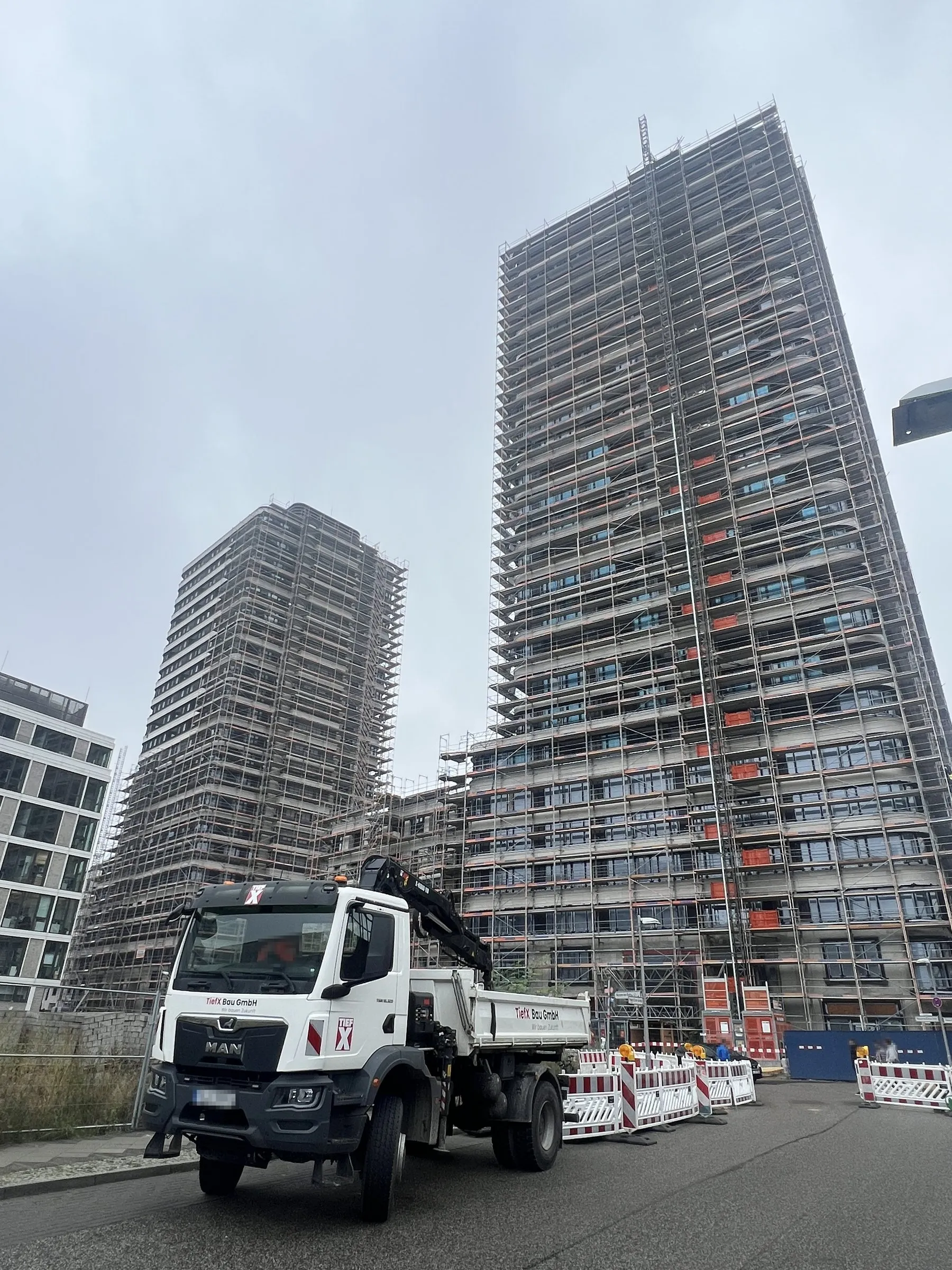 TiefX-Kipper mit Ladekran an einer abgesicherten Baustelle vor eingerüsteten Hochhäusern in Berlin