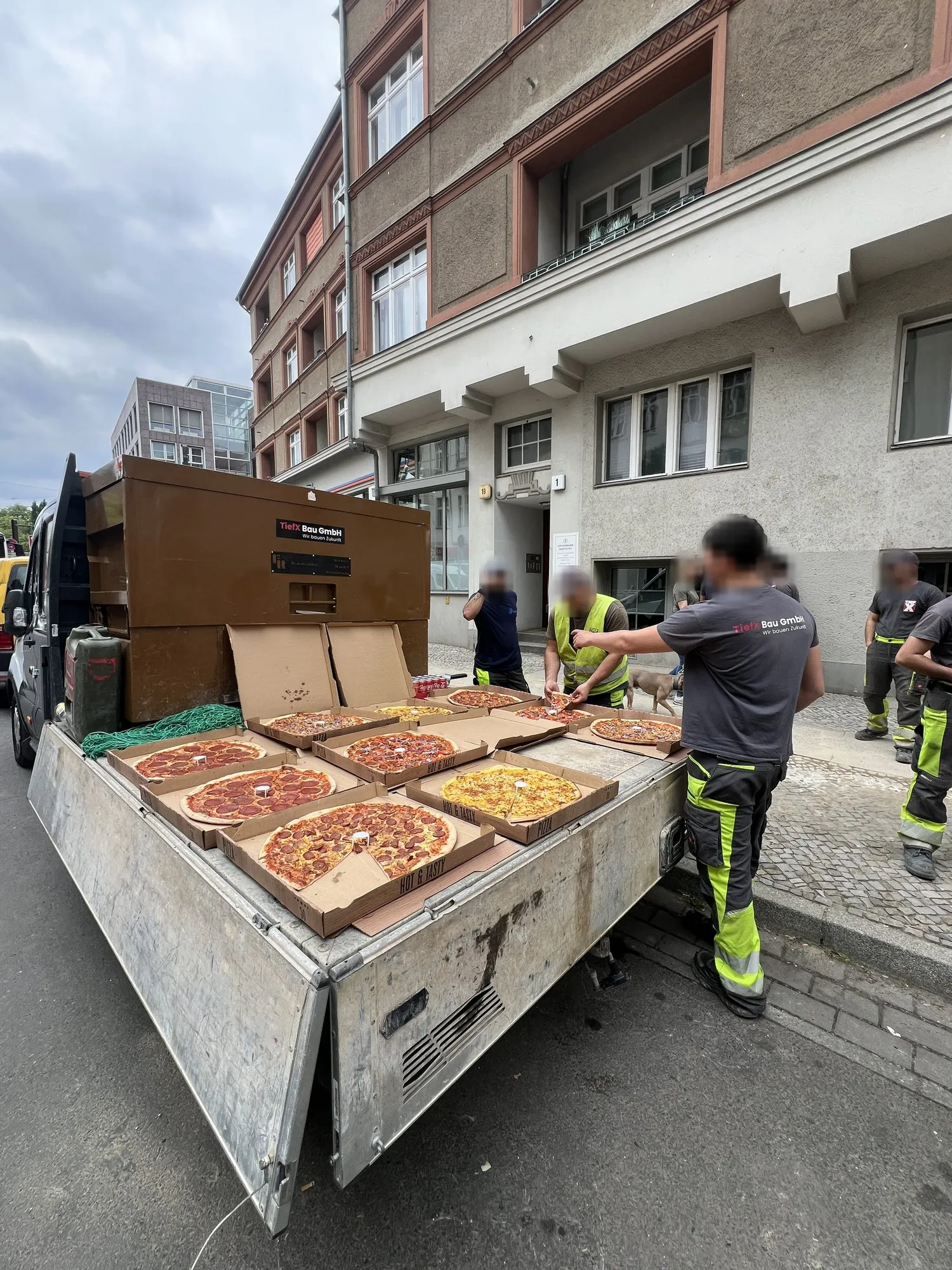 Die TiefX-Mannschaft steht in Berlin um die Ladefläche eines Transporters, auf der ein Dutzend Pizzen in offenen Kartons liegt.