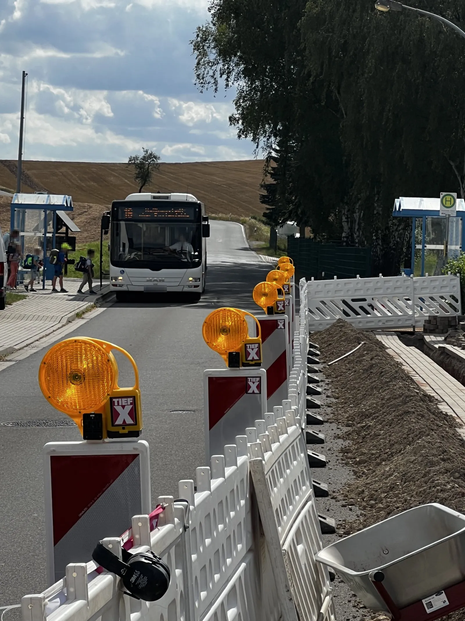 Baustellenabsicherung von TiefX: Leitbaken mit Warnleuchten und Absperrschranken entlang einer Glasfasertrasse an einer Bushaltestelle